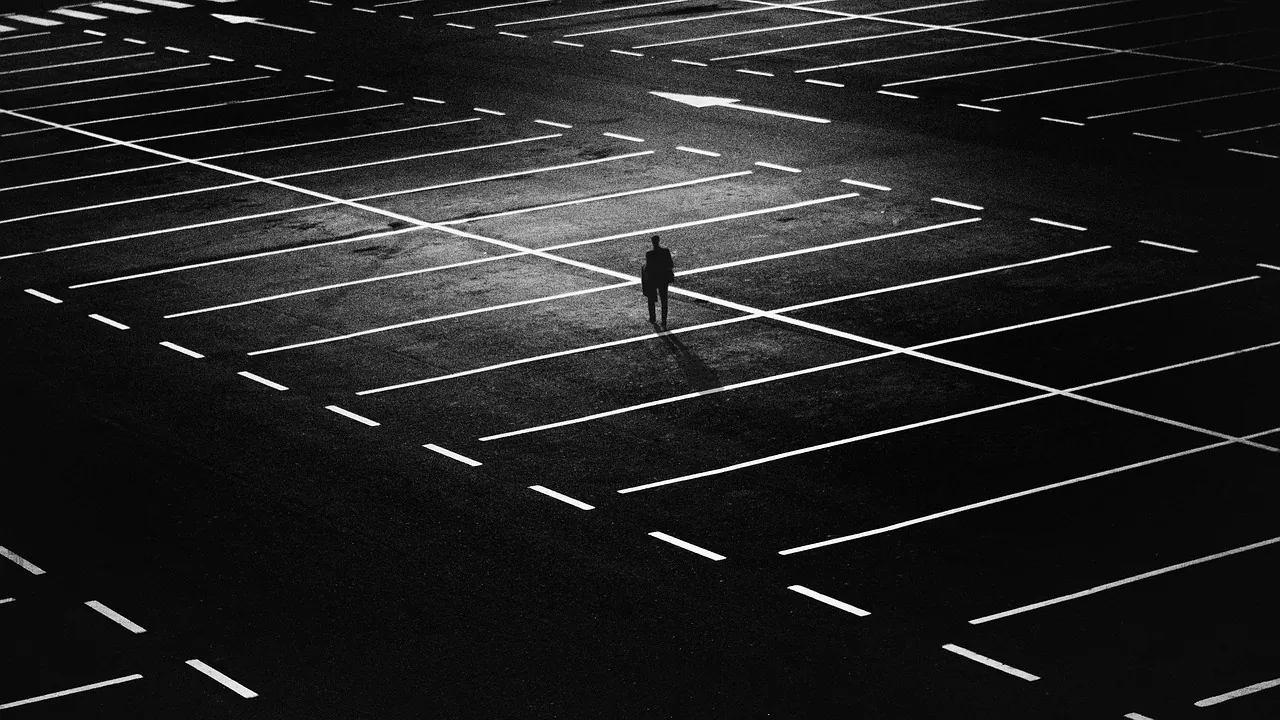 Une silhouette seule sur un parking presque vide, vue d’en haut