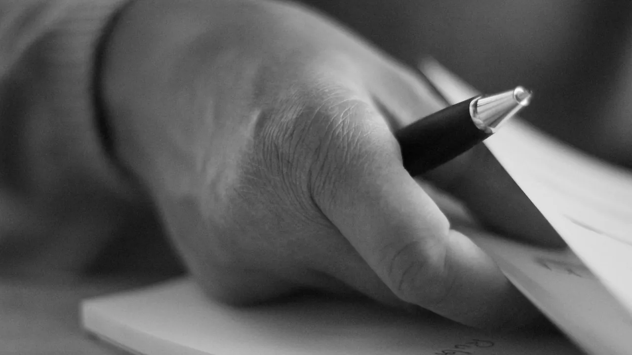 Une main écrit au stylo, en noir et blanc
