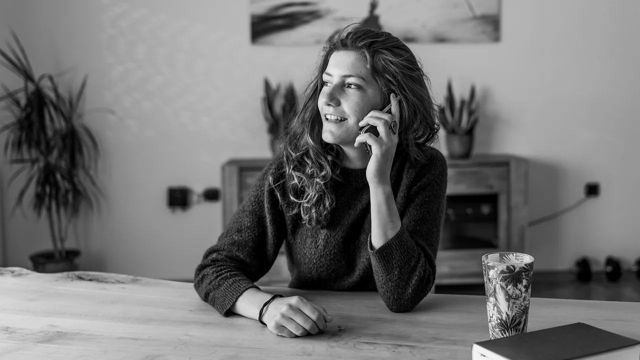 Une femme au téléphone, accoudée à un plan de travail, en noir et blanc